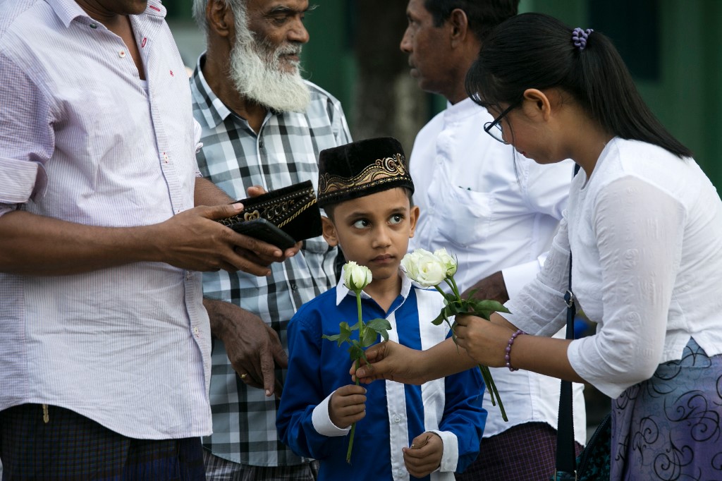 A Buddhist woman gives a white rose to a Muslim boy after he completed prayers during Eid al-Fitr at Than Lyin township on the outskirts of Yangon on June 5, 2019. (Sai Aung Main / AFP)