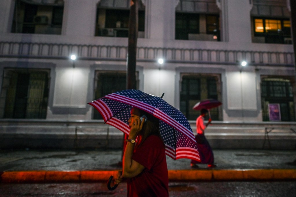 A woman holds a US flag umbrella as she talks on a phone during rainfall in Yangon. (Ye Aung Thu / AFP)