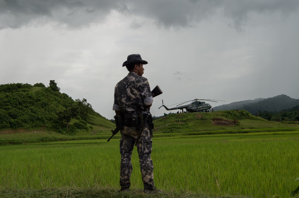 In this picture taken on September 27, 2017, a policeman stands guard near a military transport helicopter in northern Rakhine state. (STR / AFP)