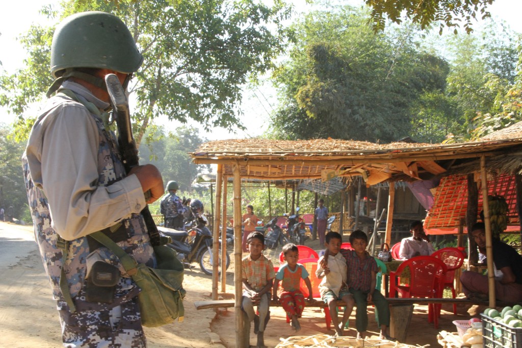 A Myanmar border guard policeman stand near a group of Rohingya Muslims in front of a small store in a village are seen during a government-organized visit for journalists in Buthidaung townships in the restive Rakhine state on January 25, 2019. (AFP)