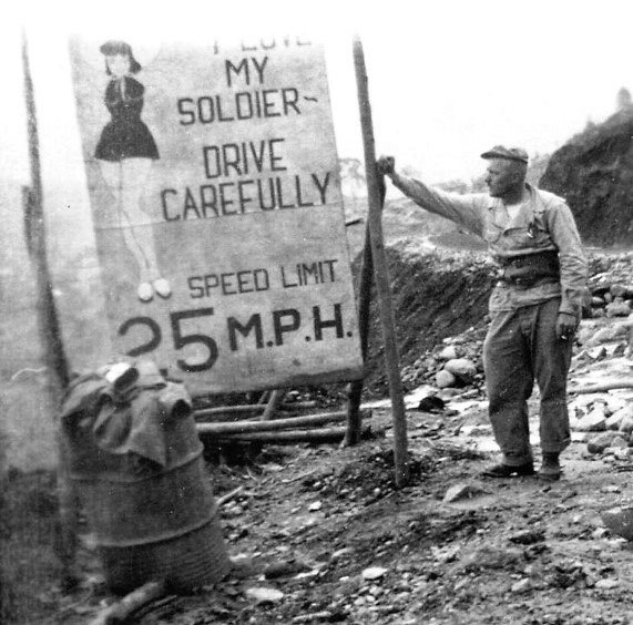 A soldier stands next to a sign on the Stilwell Road during World War Two. (CBI-Theater) 