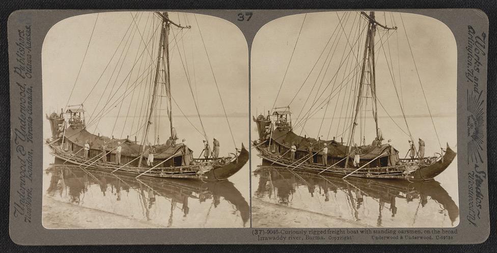 Curiously rigged freight boat with standing oarsmen, on the broad Irrawaddy River.