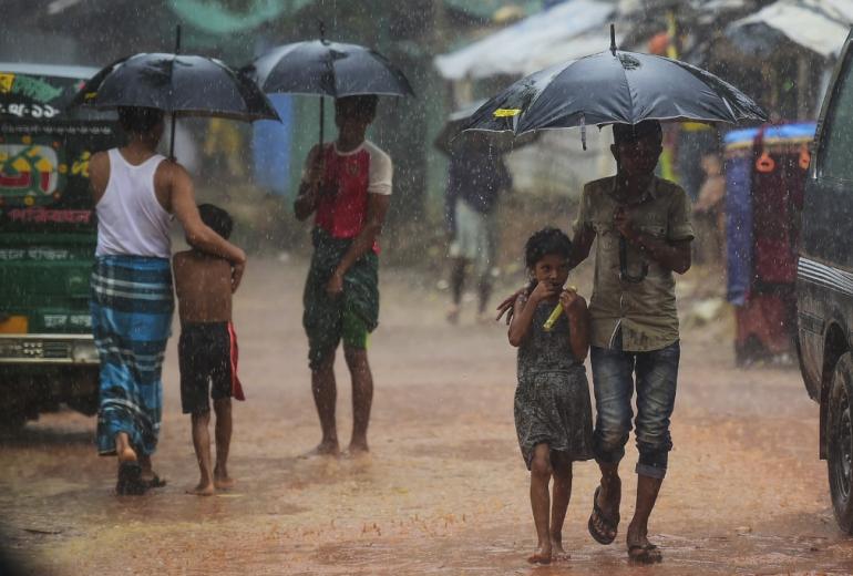 Rohingya refugees shelter under umbrellas as they walk along a path during a monsoon rainfall at Kutupalong refugee camp in Ukhia on July 23, 2019.  (Munir Uz Zaman / AFP)
