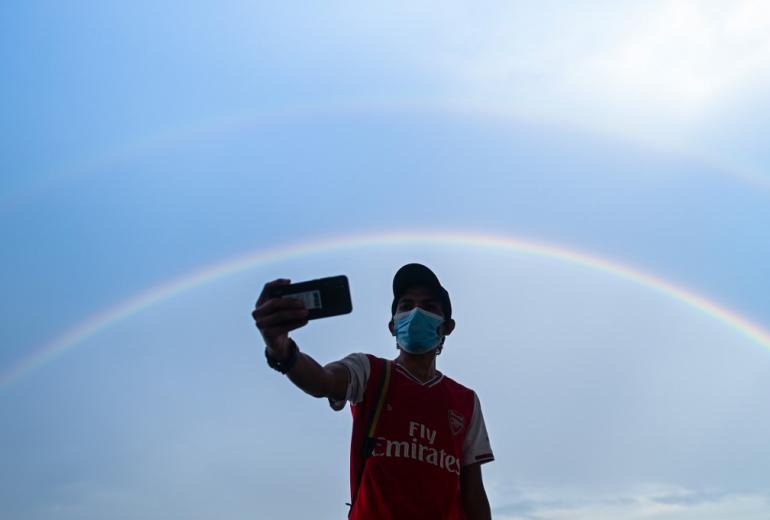 A man takes a selfie with the background of a rainbow on the sky following a rainfall in Yangon on May 1, 2020. (Ye Aung Thu / AFP)