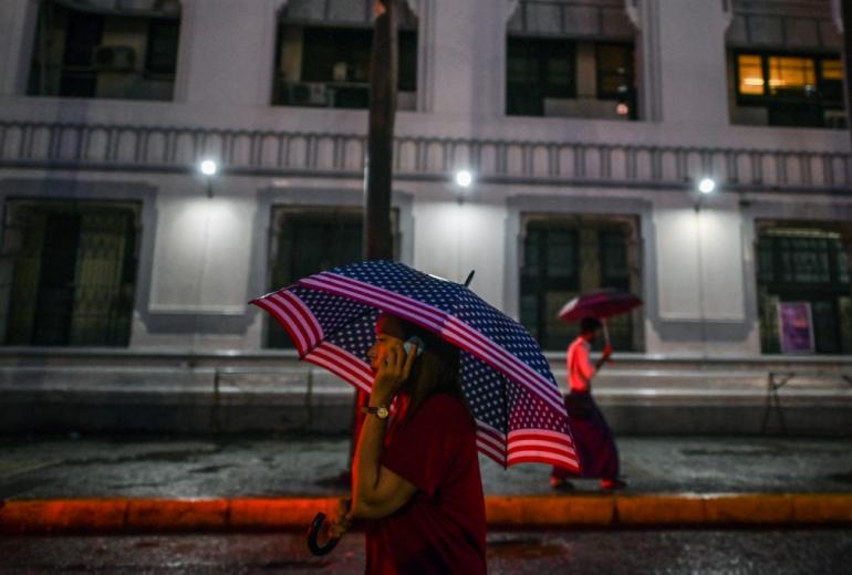 A woman holds a US flag umbrella as she talks on a phone during rainfall in Yangon. (Ye Aung Thu / AFP)