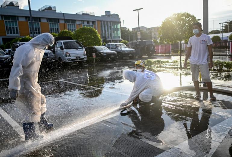 Volunteers wearing personal protective equipment (PPE) clean the frontage of Myanmar Expo Hall converted as "Happy Covid Center" for people infected with Covid-19 in Yangon. (Ye Aung Thu / AFP)