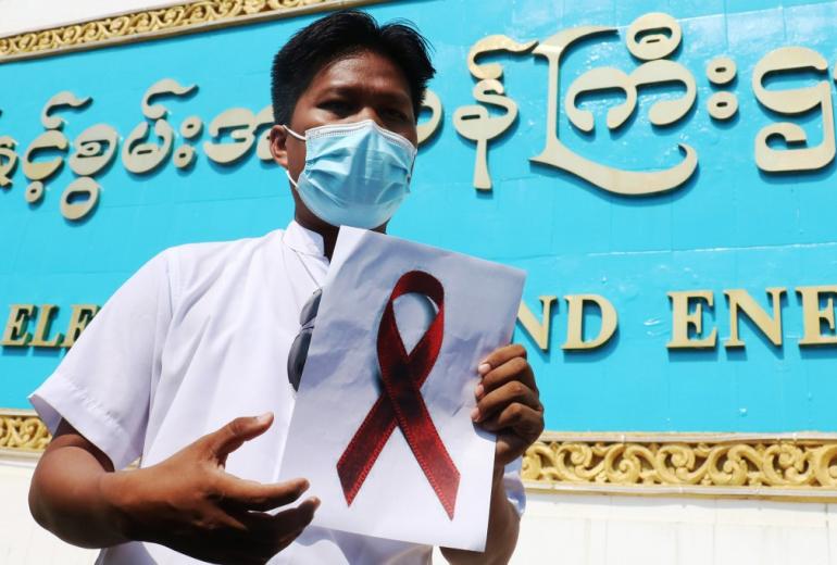 A staff member of the Ministry of Electricity and Energy holds a sign with a red ribbon during a protest against the military coup in Naypyidaw on February 5, 2021. (STR / AFP)