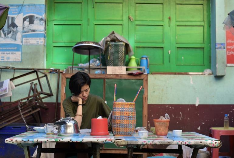 A young woman (unrelated to our reader below) reads a newspaper as she has breakfast in a street in Yangon. (AFP / Nicolas Asfouri) 
