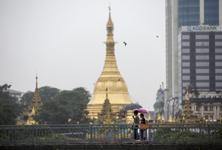 A woman (right) wears a face mask whilst walking with a friend past Sule Pagoda in Yangon on July 26, 2017. (Aung Kyaw Htet / AFP)