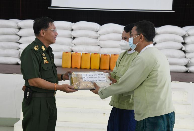 Min Aung Hlaing spreads goodwill with a bag of rice, an apparent bracelet magic protection and a gun. (Global New Light of Myanmar) 