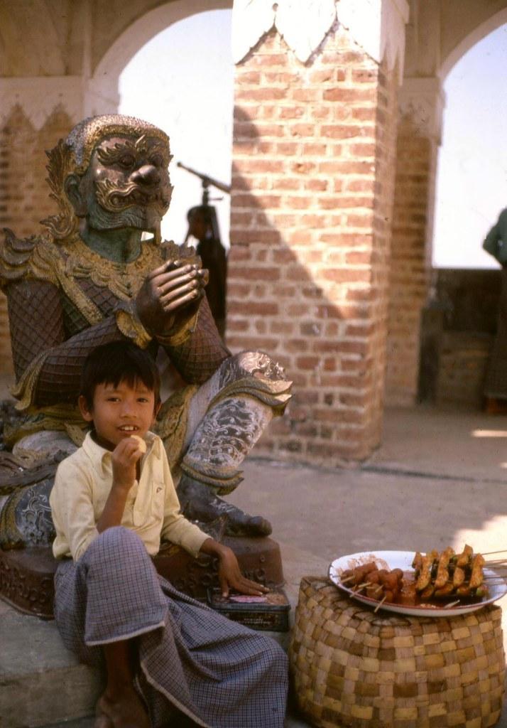 A boy sits down next to some meat skewers in Mandalay.
