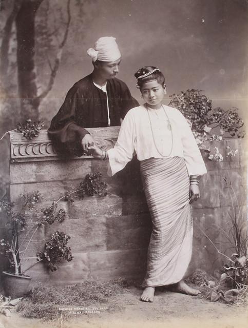 A Burmese man holds hands with a girl, who seems slightly disaffected. (1906)