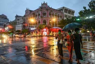This photo taken on June 14, 2020 shows people holding umbrellas as they cross a road during rainfall in Yangon. (Ye Aung Thu / AFP)