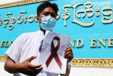 A staff member of the Ministry of Electricity and Energy holds a sign with a red ribbon during a protest against the military coup in Naypyidaw on February 5, 2021. (STR / AFP)