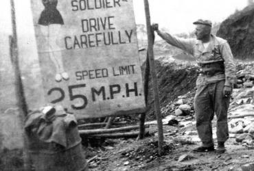 A soldier stands next to a sign on the Stilwell Road during World War Two. (CBI-Theater) 