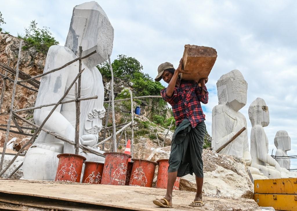 A worker carries a log as he walks past marble statues being chiselled in Sagyin village. (Ye Aung Thu / AFP)