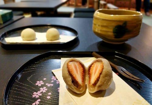 Strawberry daifuku in front of chocolate mochi and a bowl of matcha green tea. (Myanmar Mix)