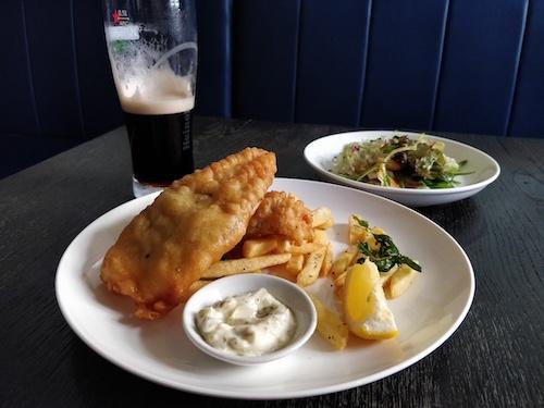 Fish and chips and a glass of Guiness, with reupholstered leather benches in the background.